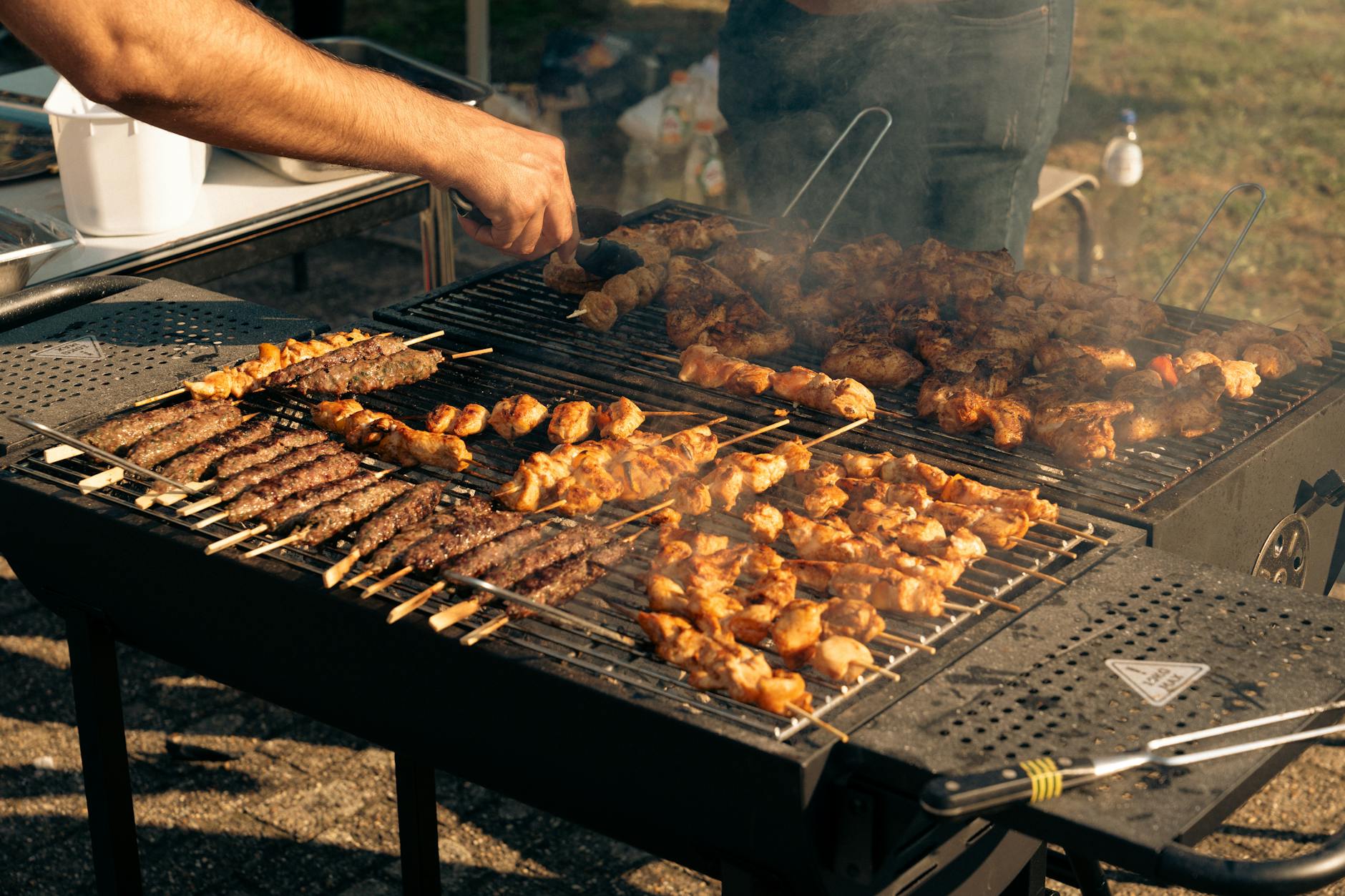 A variety of skewered meats being grilled on an outdoor barbecue. Perfect for summer gatherings. (Photo by Ines M. on Pexels)